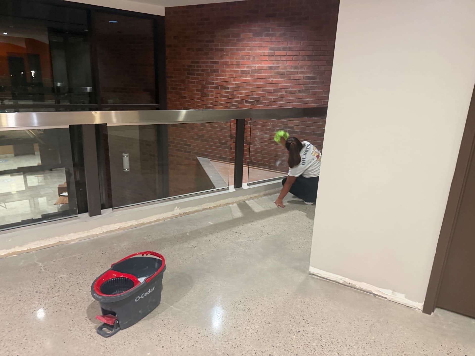 Hello Clean & Company crew member hand-detailing glass railing and floor edges during a commercial construction cleanup in Lakewood, CO